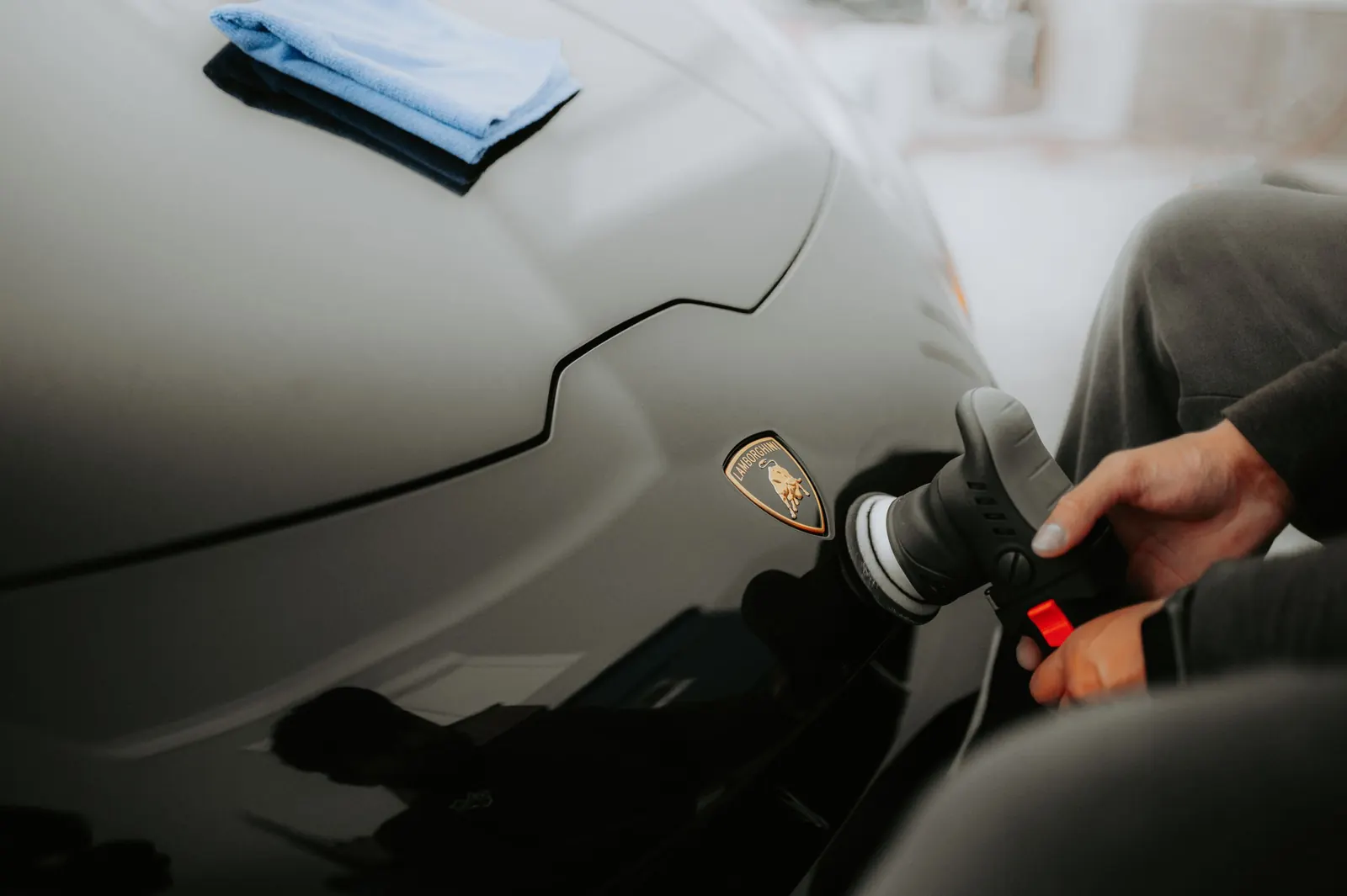 An installer machine-polishing a gray sports car